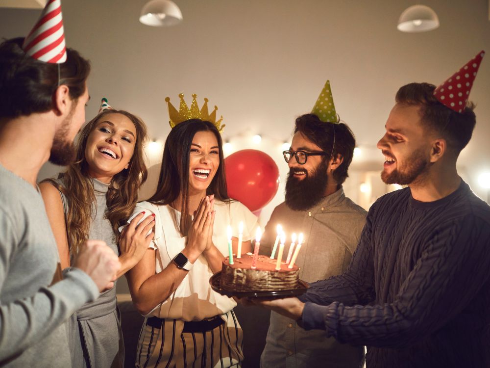 A smiling woman is presented with a birthday cake