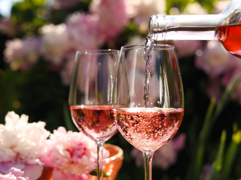 Rose wine being poured into a wine glass with flowers in the background